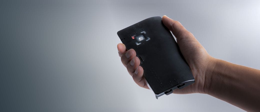 A hand holds a black portable projector with a visible lens and buttons.