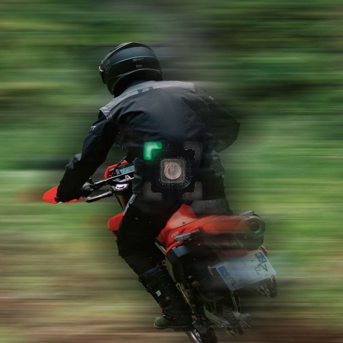 Motorcyclist on a dirt bike speeds through a green, blurred forest trail.