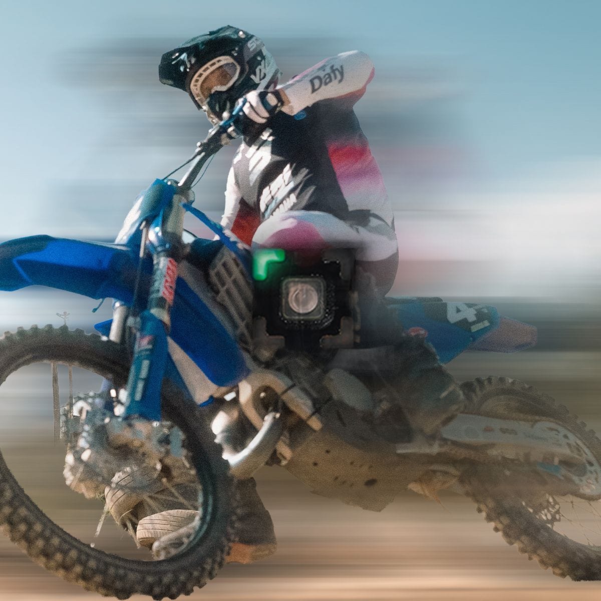 Dirt bike rider in full gear speeds across a sandy track, motion blur.
