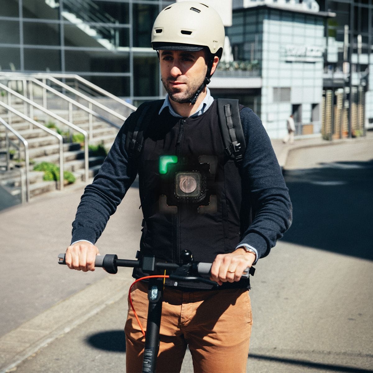 Man with helmet and smart vest on an electric scooter with a green arrow.