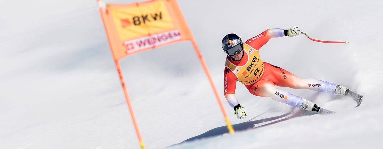 A professional skier in a red suit races down a snowy slope past orange gates.