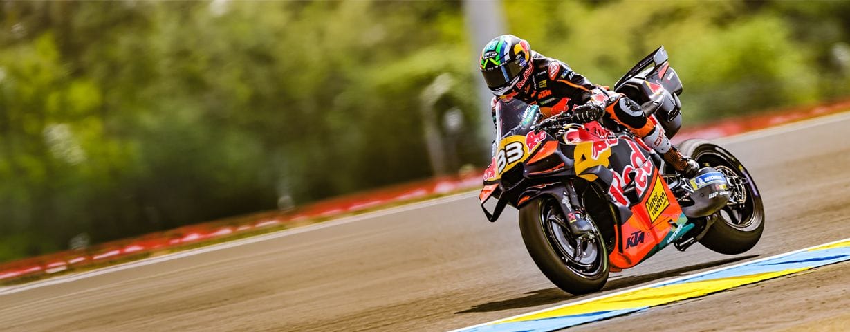A motorcycle racer in colorful gear leans sharply into a turn on a track.