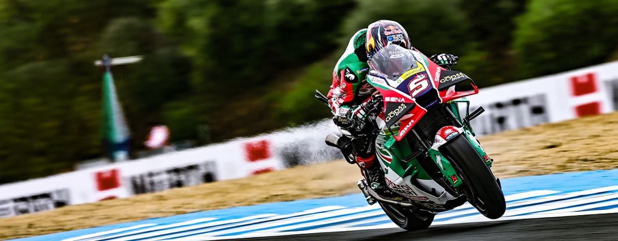 Racer on a green and red motorcycle leans into a turn on a track.