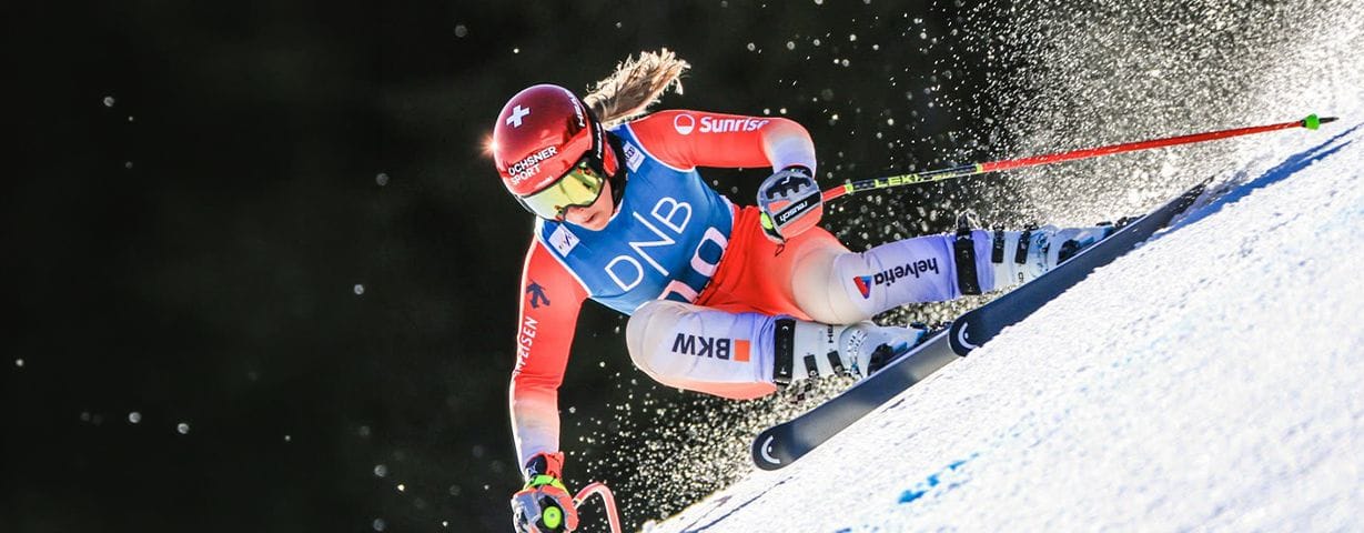 Female alpine skier in red suit carves a turn down a snowy mountain.
