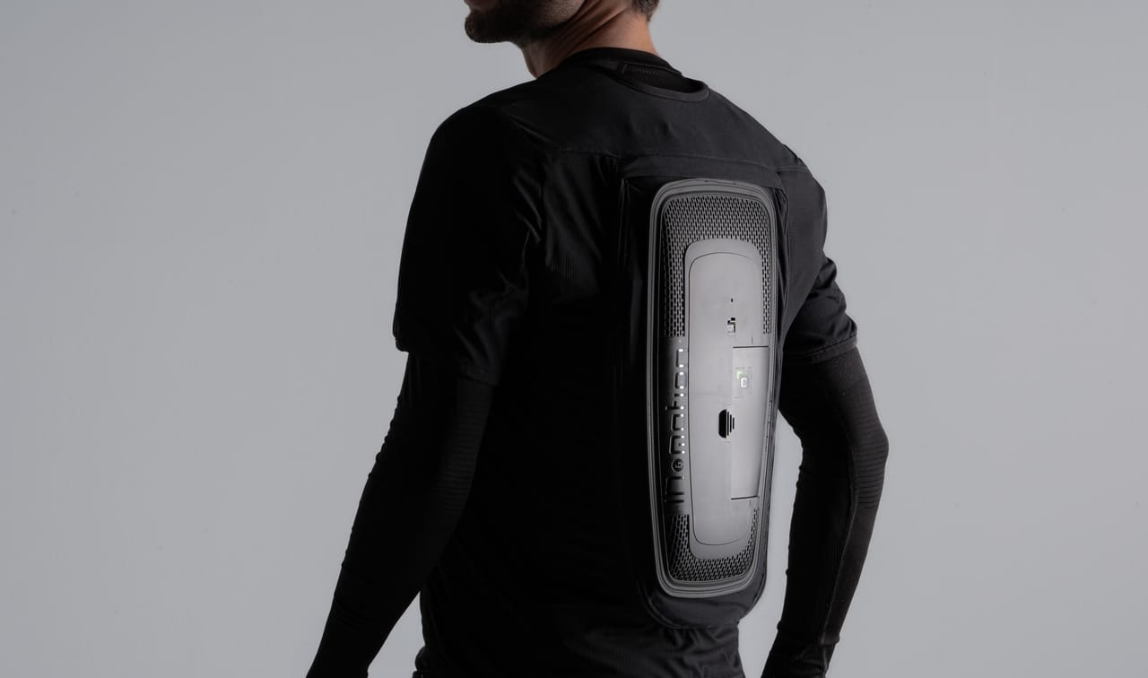 Man wearing a black shirt with a sleek, rectangular tech device on his back.