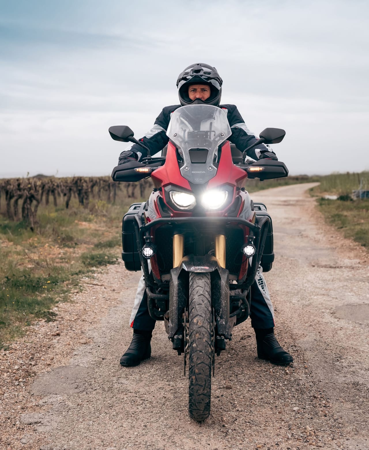 Person in motorcycle gear on a red adventure bike on a dirt path.