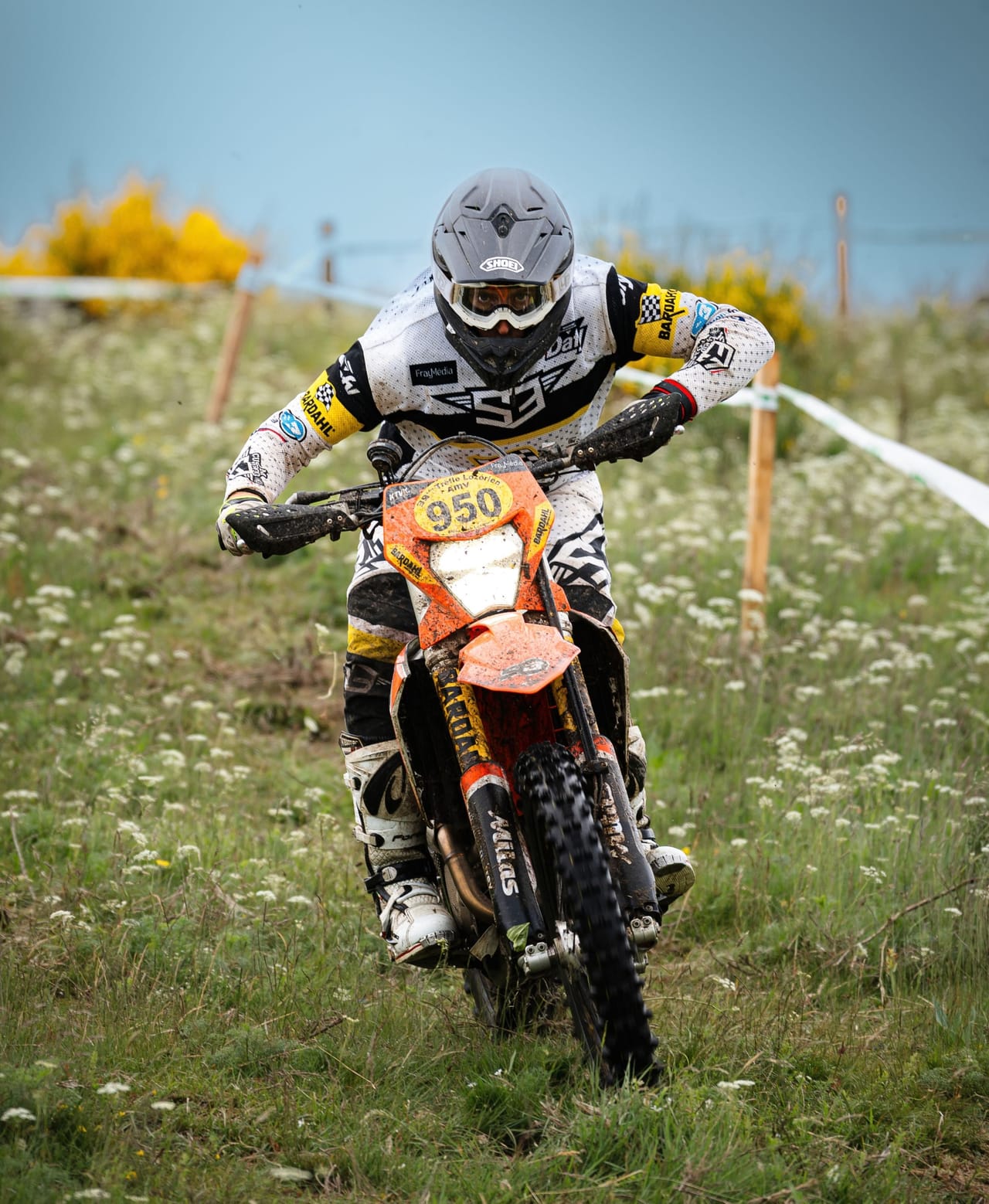 Motorcyclist on an orange dirt bike races through a grassy field.