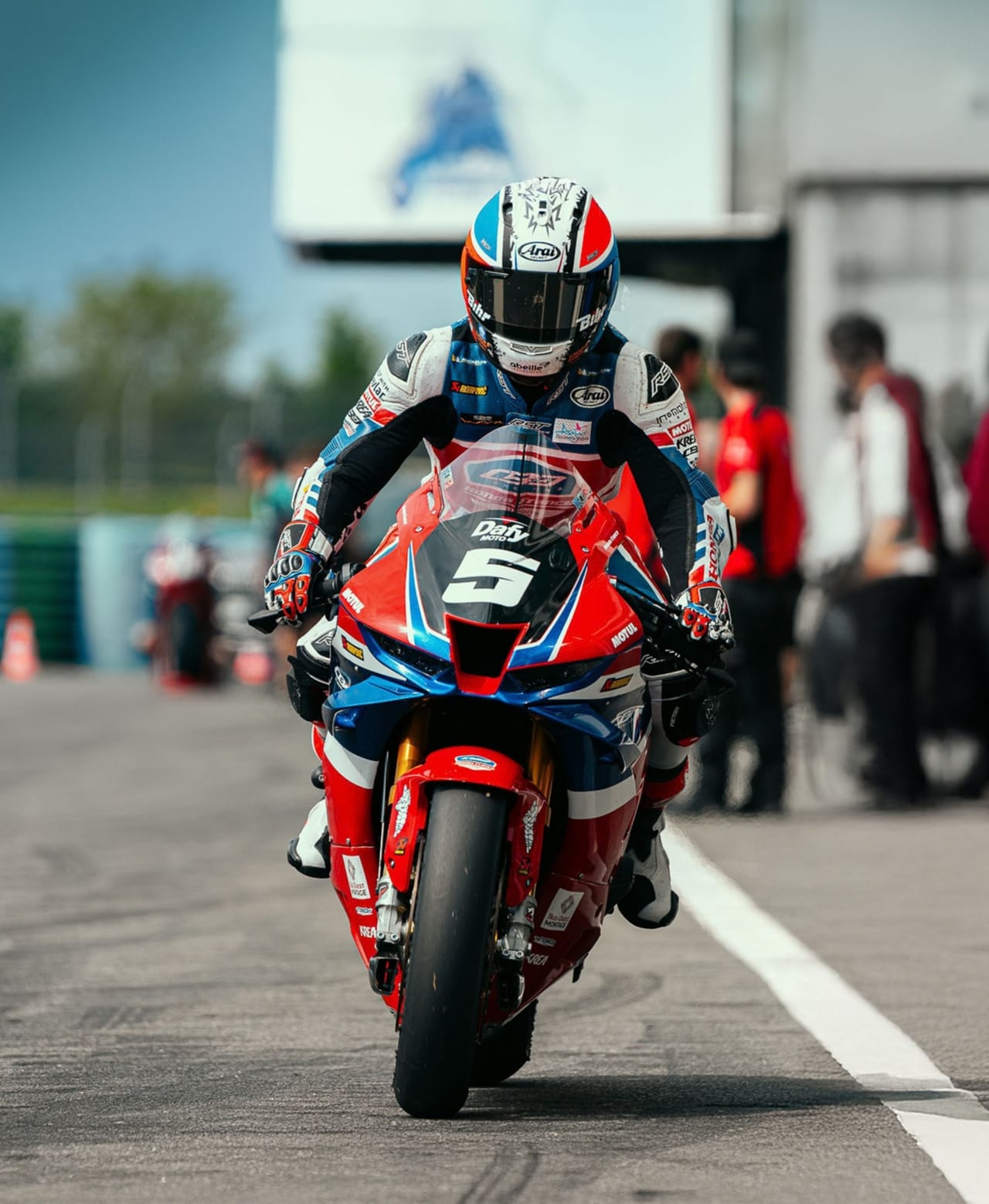 A racer on a red and blue motorcycle with number 5 ready to race.