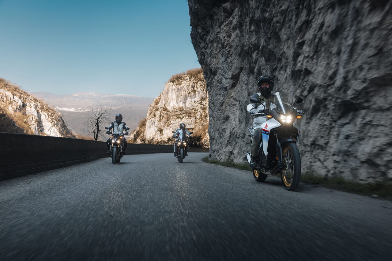 Three people riding motorcycles on a winding mountain road next to a rocky cliff.