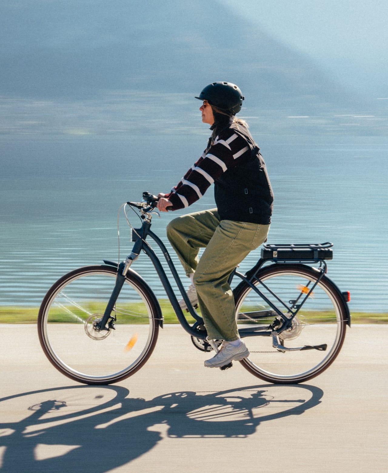 Person in helmet riding an e-bike along a scenic waterside path.