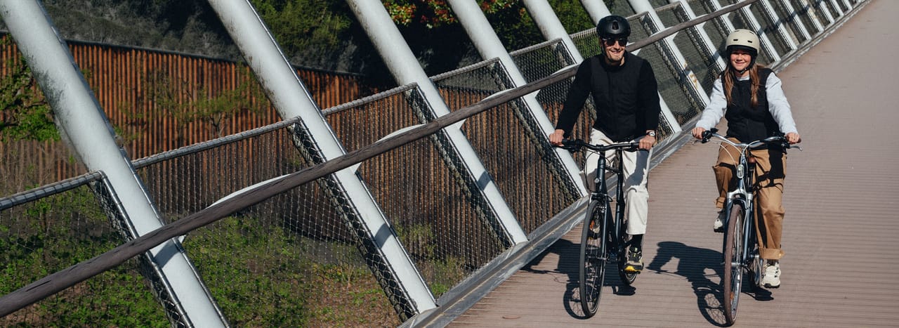 Two people riding bicycles on a modern bridge with diagonal railings.