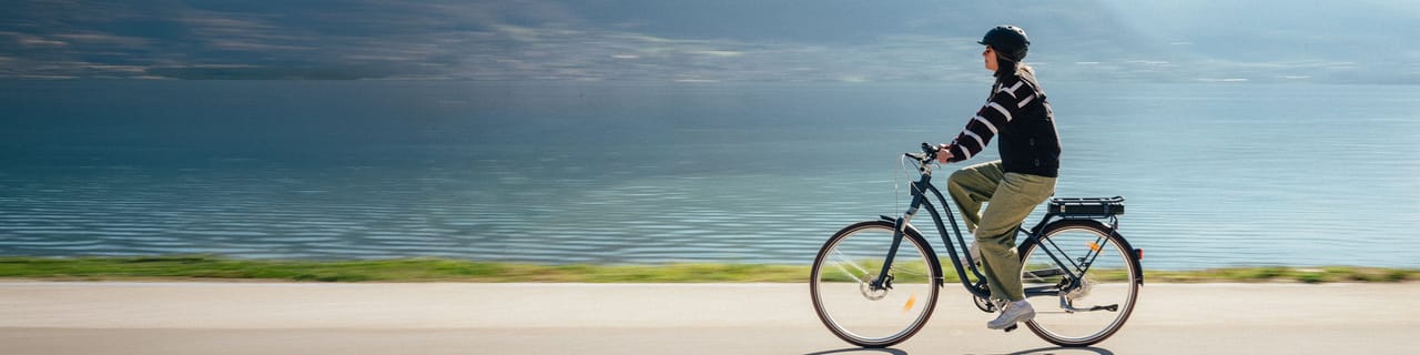 Person riding a bicycle on a sandy beach next to the ocean under a cloudy sky.