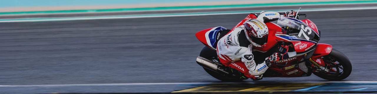 A motorcyclist on a red and white bike leans into a turn on a race track.
