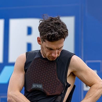 Man in a black sleeveless top adjusting a hexagonal padded protective vest.